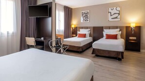 Une chambre d’hôtel avec un grand lit, deux petits lits, un bureau avec une chaise, un téléviseur à écran plat et des œuvres d’art accrochées aux murs.