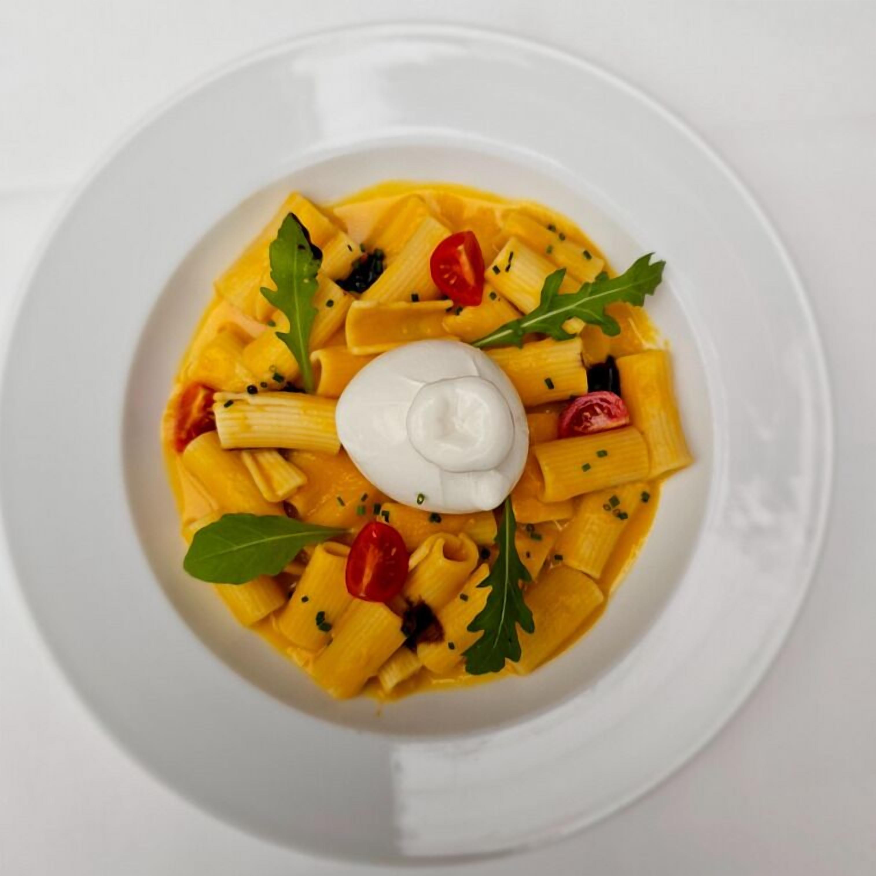 Un plato blanco con pasta, tomates cherry, rúcula y una cucharada de crema.