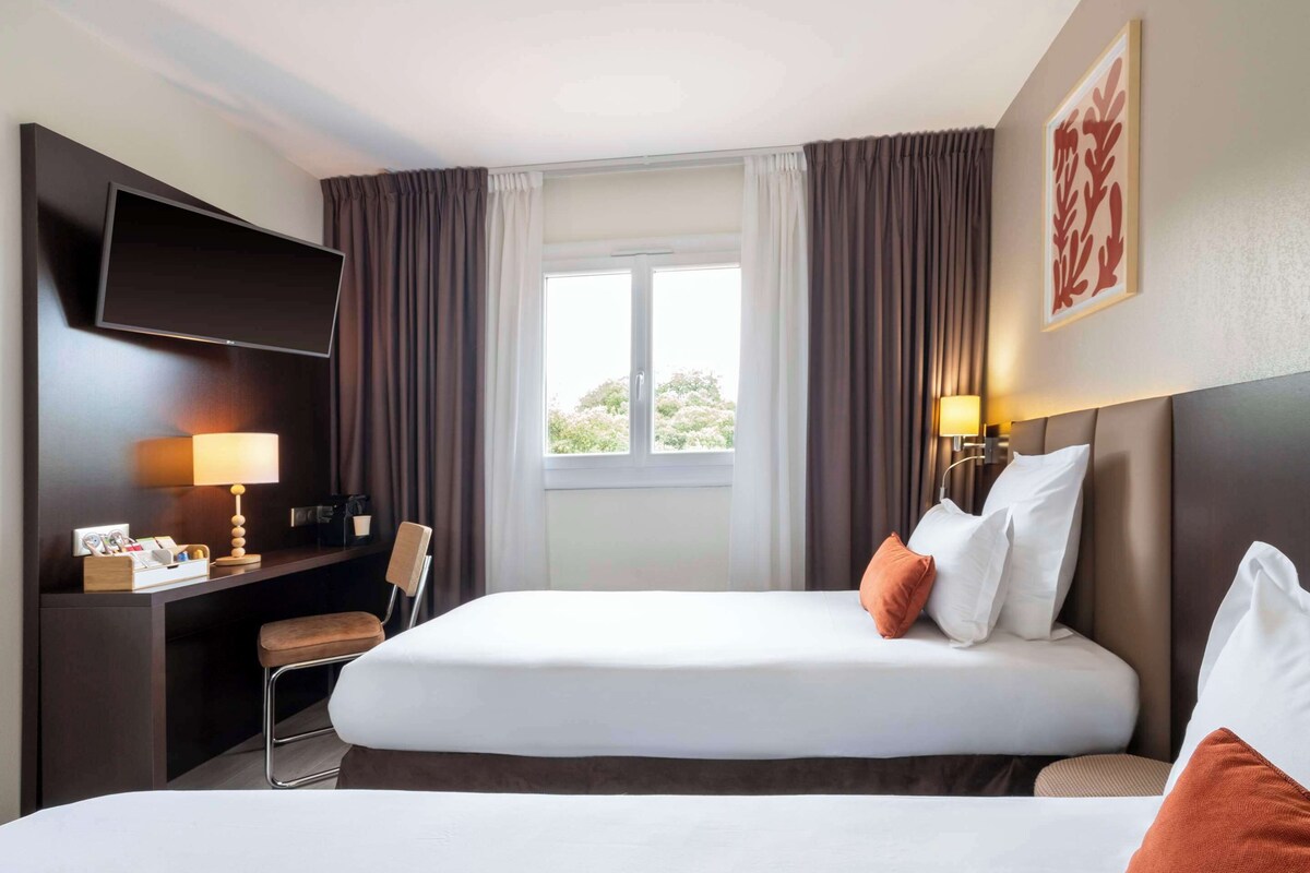Une chambre d’hôtel avec un grand lit, un bureau doté d’un téléviseur à écran plat, une chaise et une fenêtre avec des rideaux.
