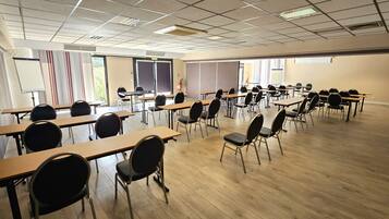 Un salón de conferencias con varias mesas y sillas, una pizarra y una pantalla de proyector.