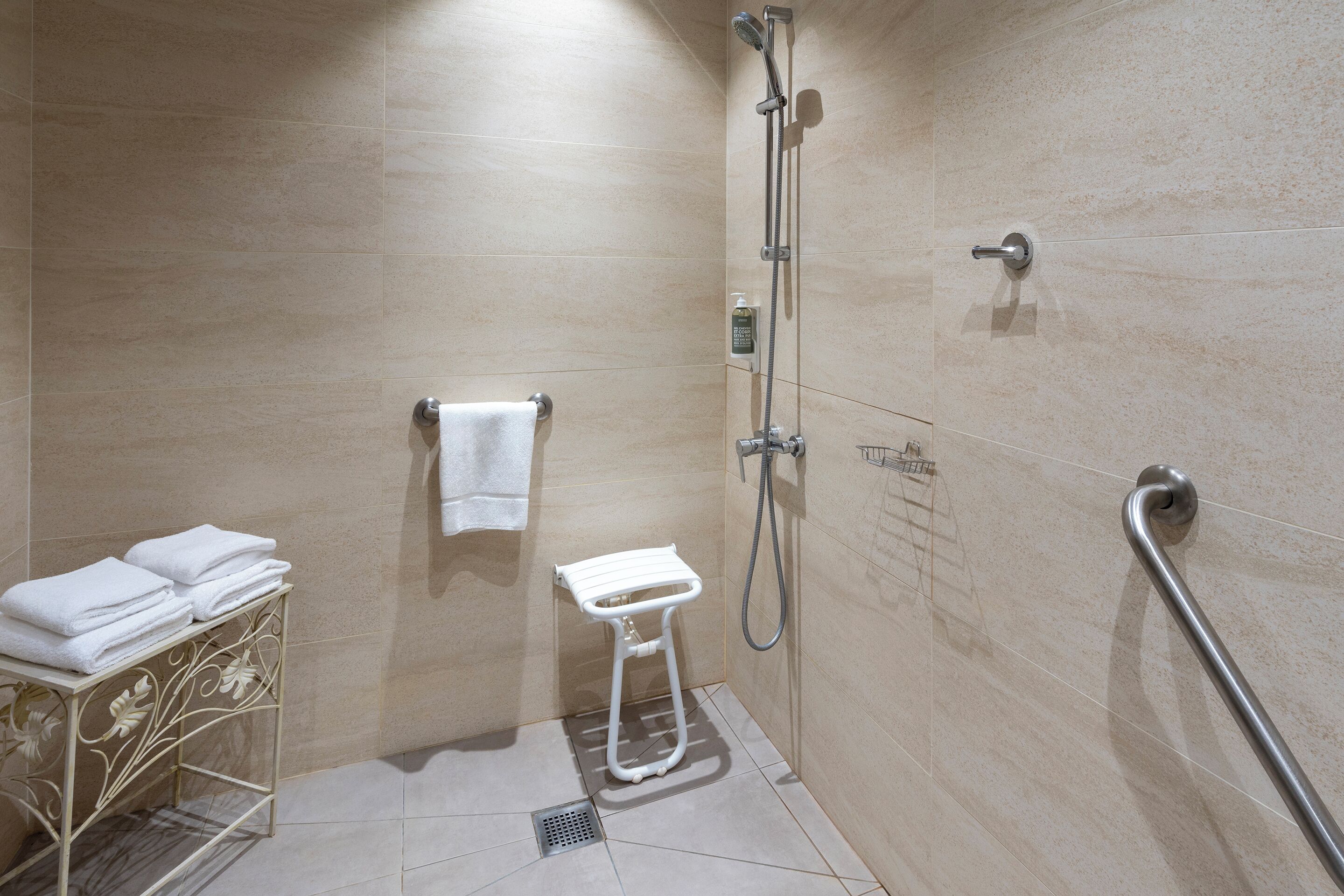Un baño moderno con ducha, un pequeño banco blanco, un perchero y una barra de apoyo.