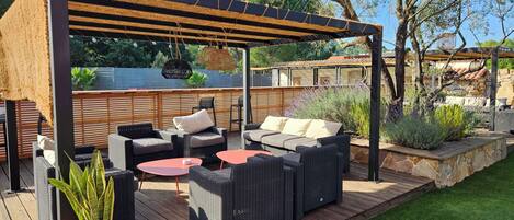 A covered outdoor seating area with wicker furniture and a small table, surrounded by a wooden deck and a stone wall.