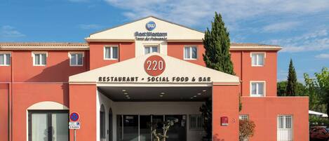 A Best Western hotel entrance with a sign indicating 220 rooms, a restaurant, social food & bar, and a parking area with 2 places.
