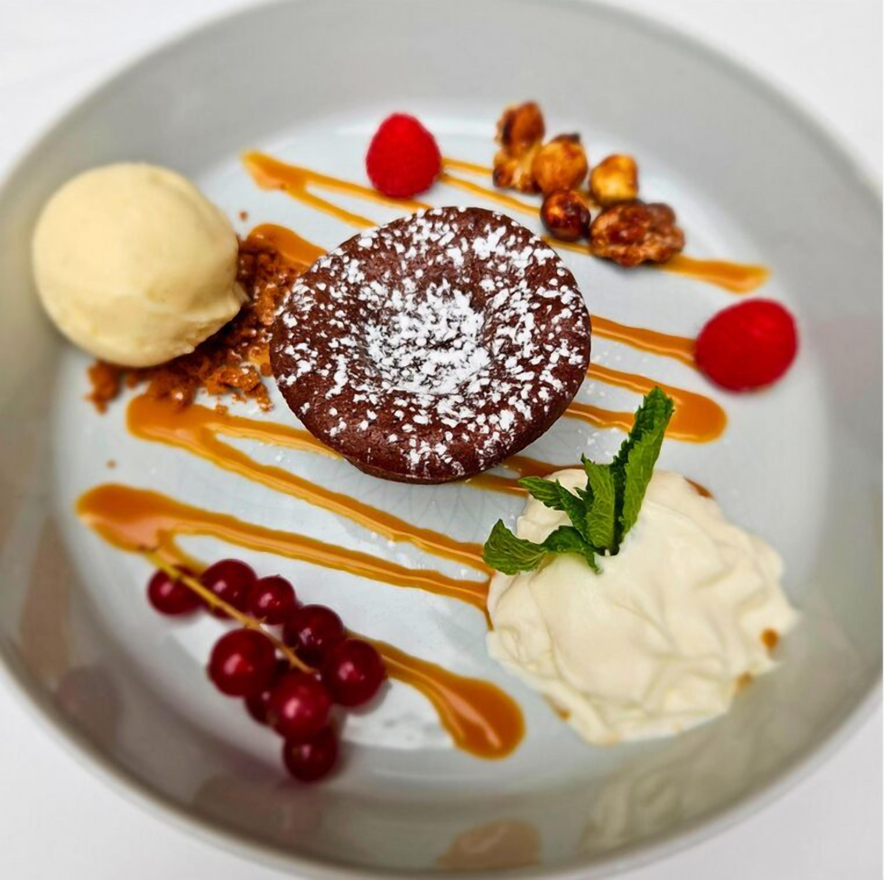 Un plato de postre con pastel de chocolate, helado, salsa de caramelo, bayas rojas y nueces.