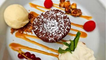 Un plato de postre con pastel de chocolate, helado, salsa de caramelo, bayas rojas y nueces.