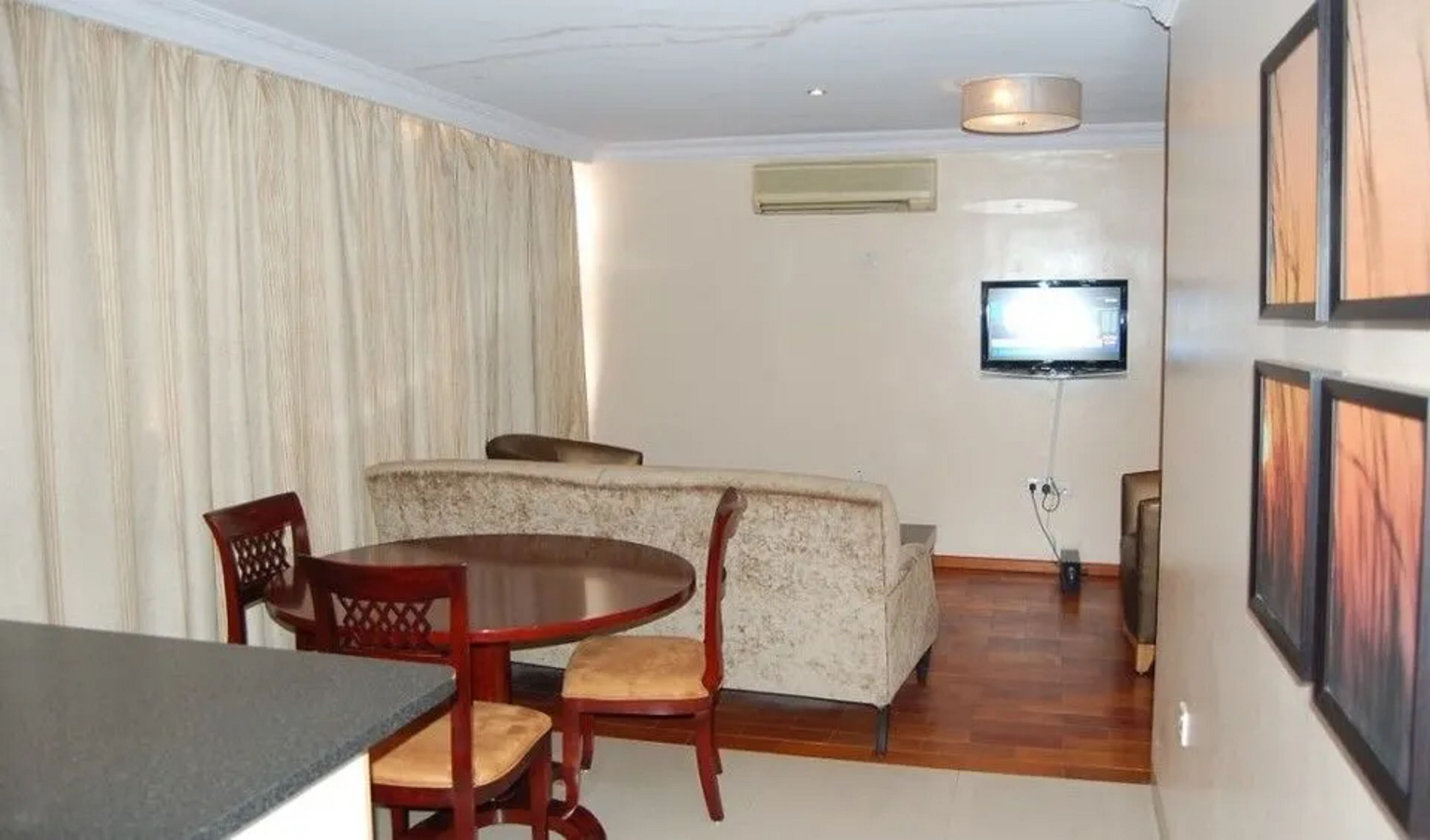 A compact living space with a dining area, a sofa, a TV mounted on the wall, and a small table.