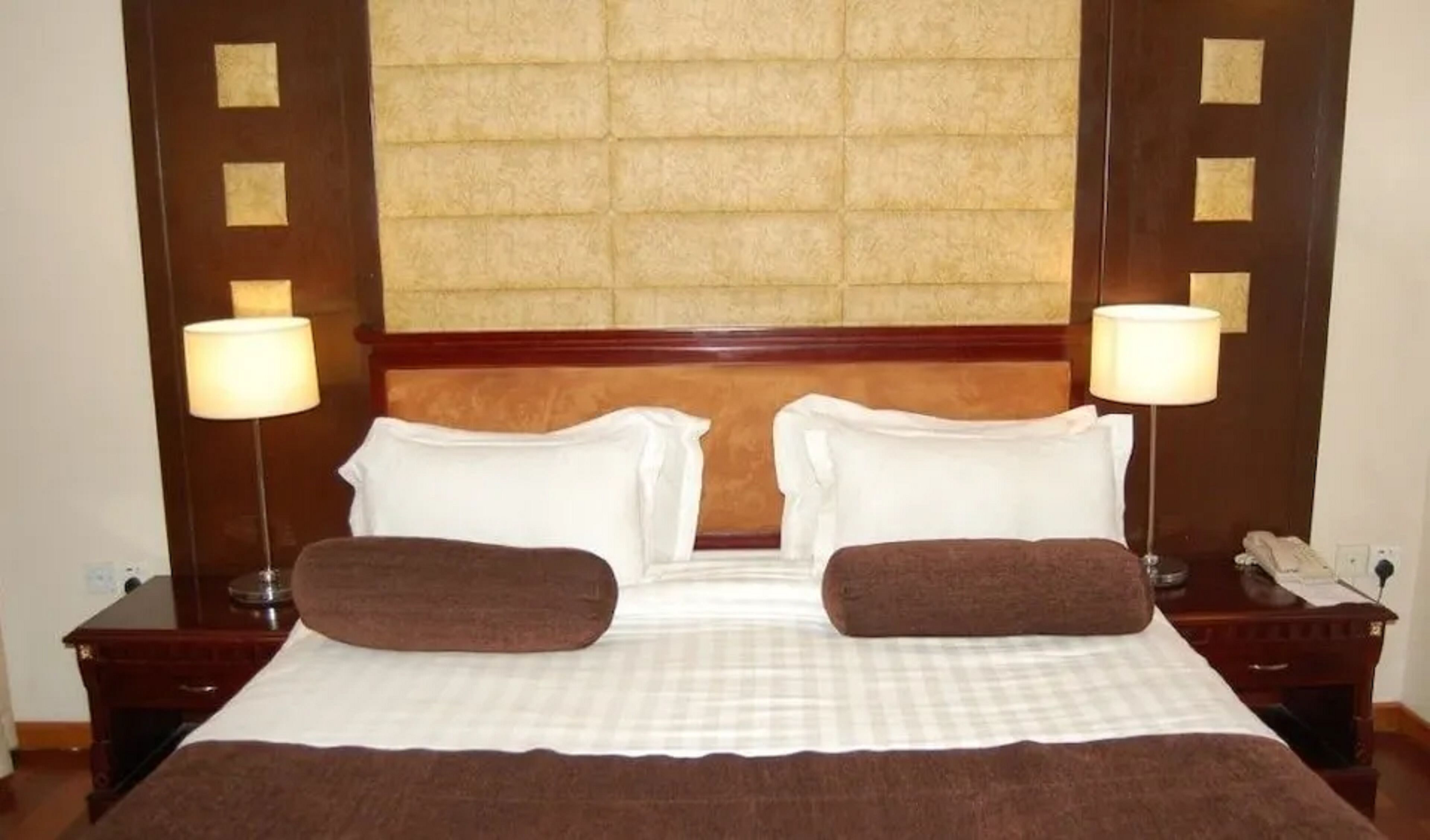 Une chambre d’hôtel avec un grand lit, deux tables de chevet, une tête de lit et deux lampes.