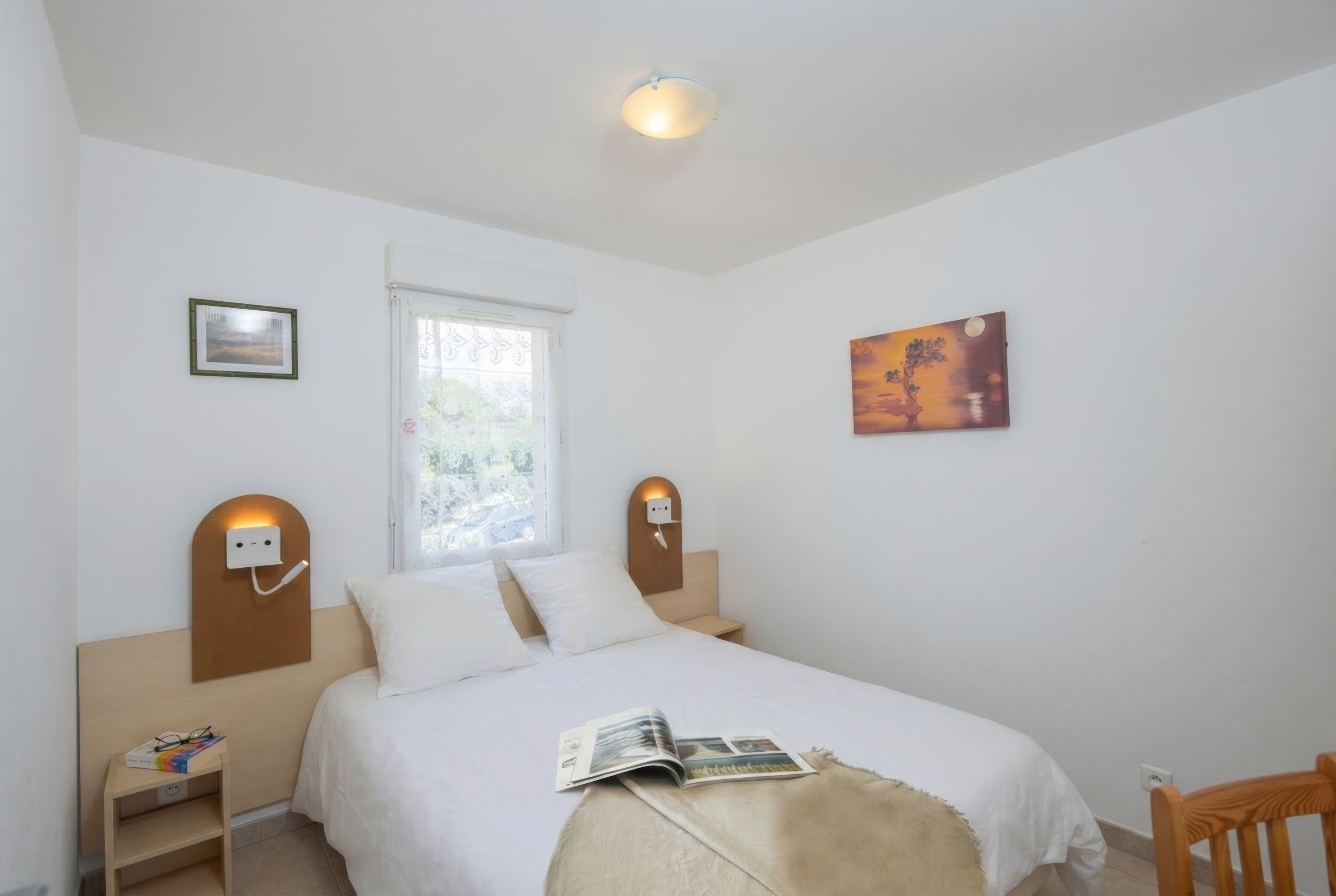 A bedroom with a bed, bedside tables, a window, and wall-mounted artwork.