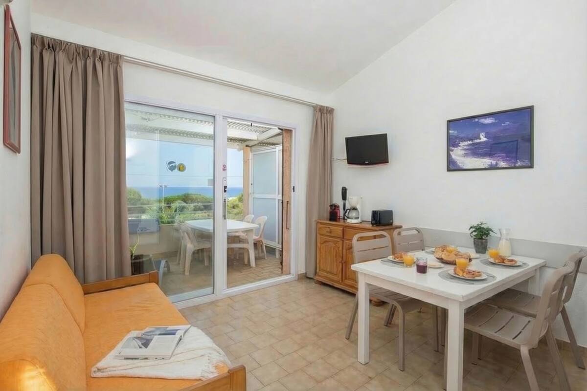 Una habitación con sofá, una mesa de comedor con desayuno, televisor y puerta corrediza de vidrio a un área exterior.