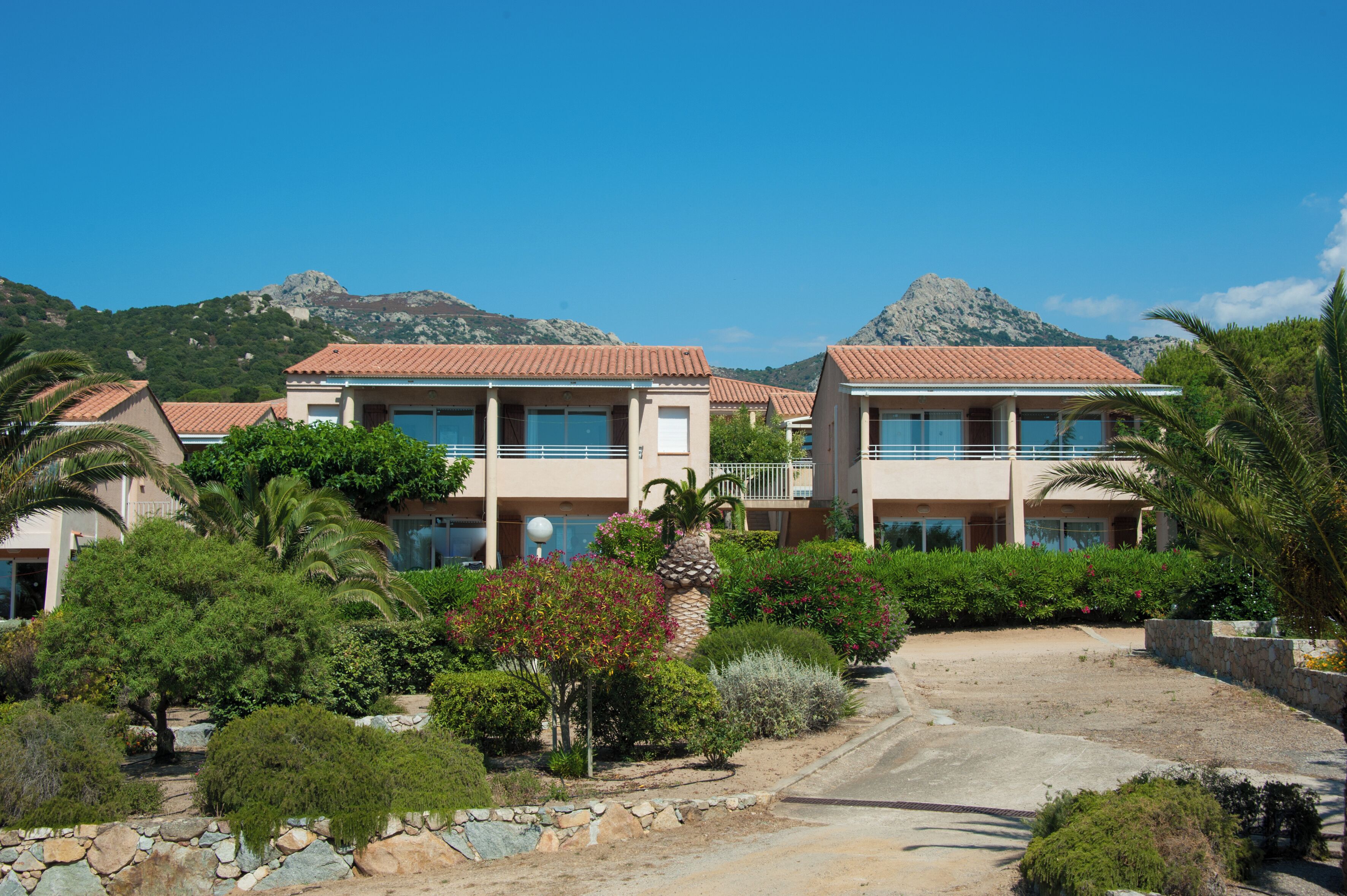 A two-story building with a red-tiled roof, surrounded by lush greenery and a mountainous backdrop.