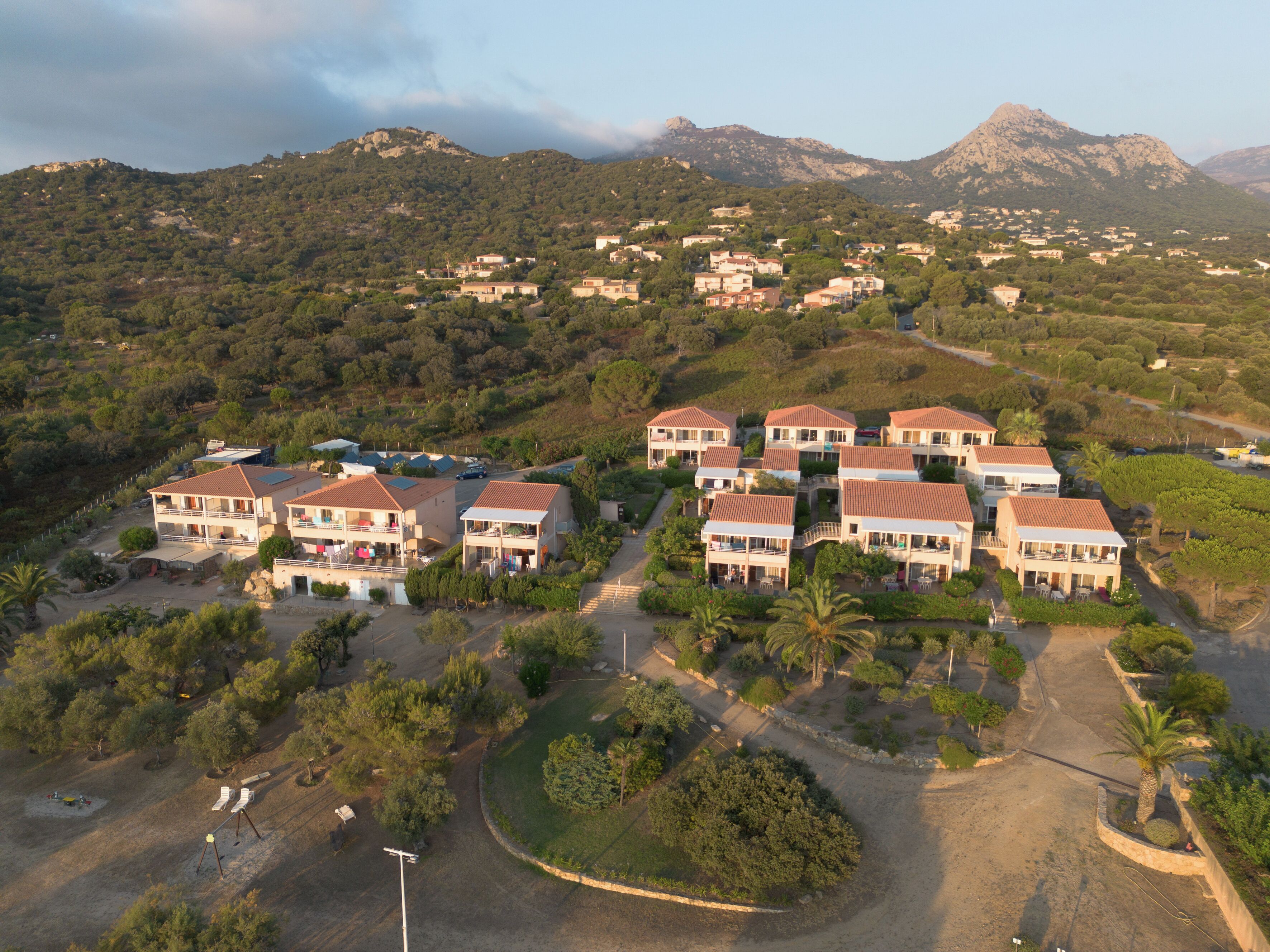 A residential area with multiple two-story houses, a winding road, and a mountainous backdrop.