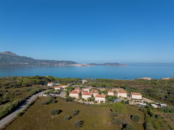 A coastal residential area with houses, a road, and a clear view of the sea and distant mountains. - Résidence Pierre & Vacances Arinella (Lumio)