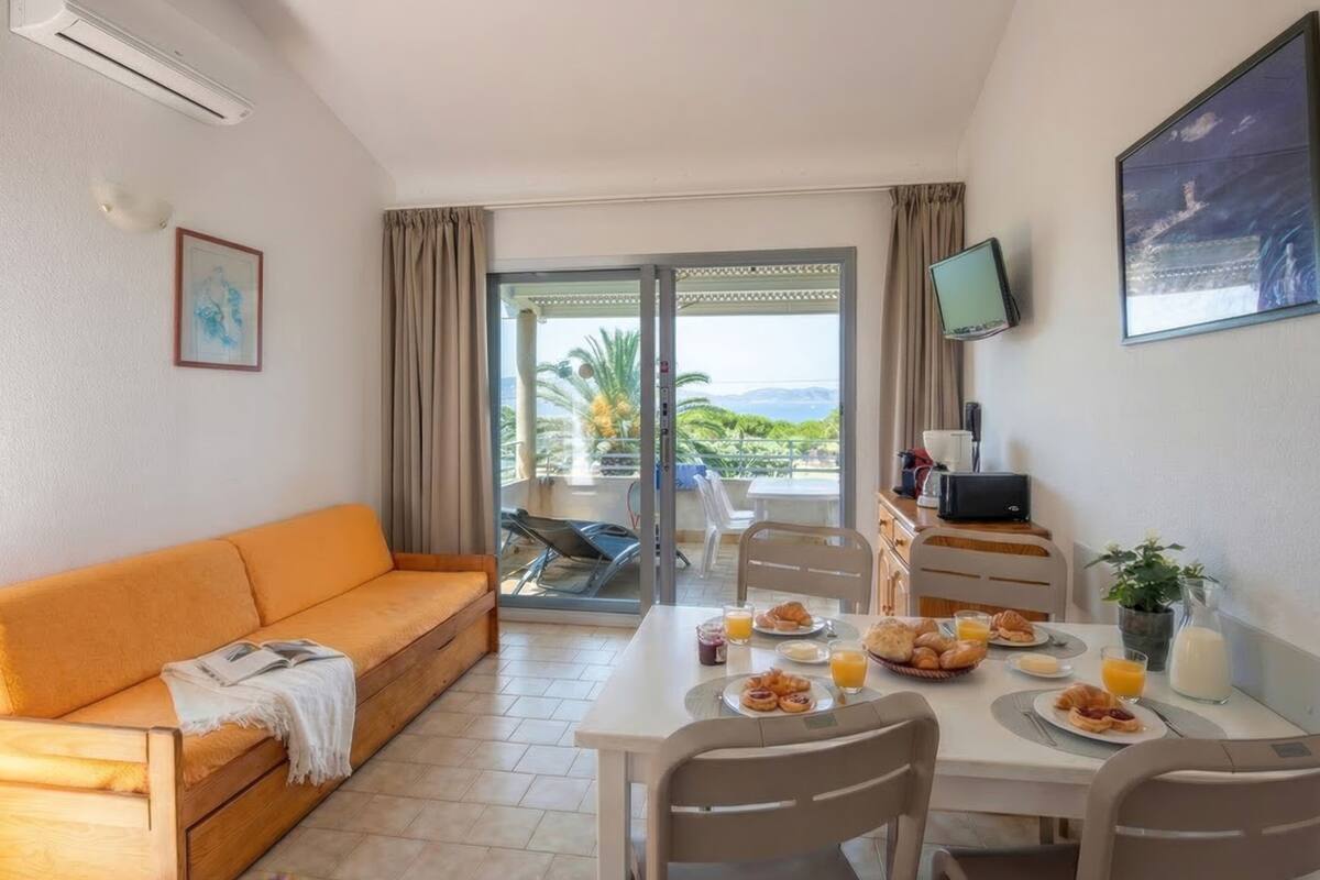 Habitación con sofá, mesa de comedor, zona de desayuno, televisor y vista a través de una puerta corredera.