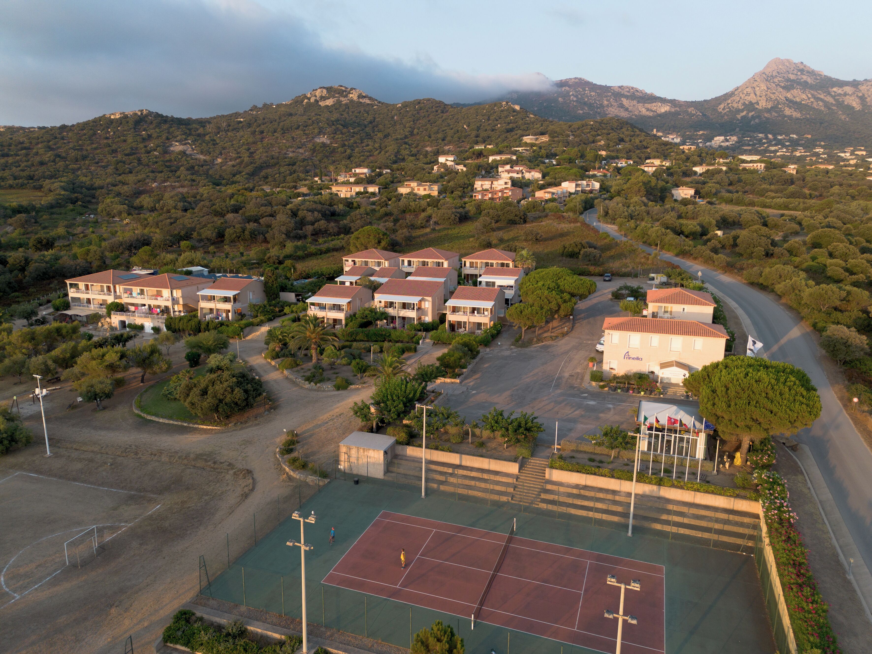 A residential area with houses, a tennis court, and a mountain in the background.