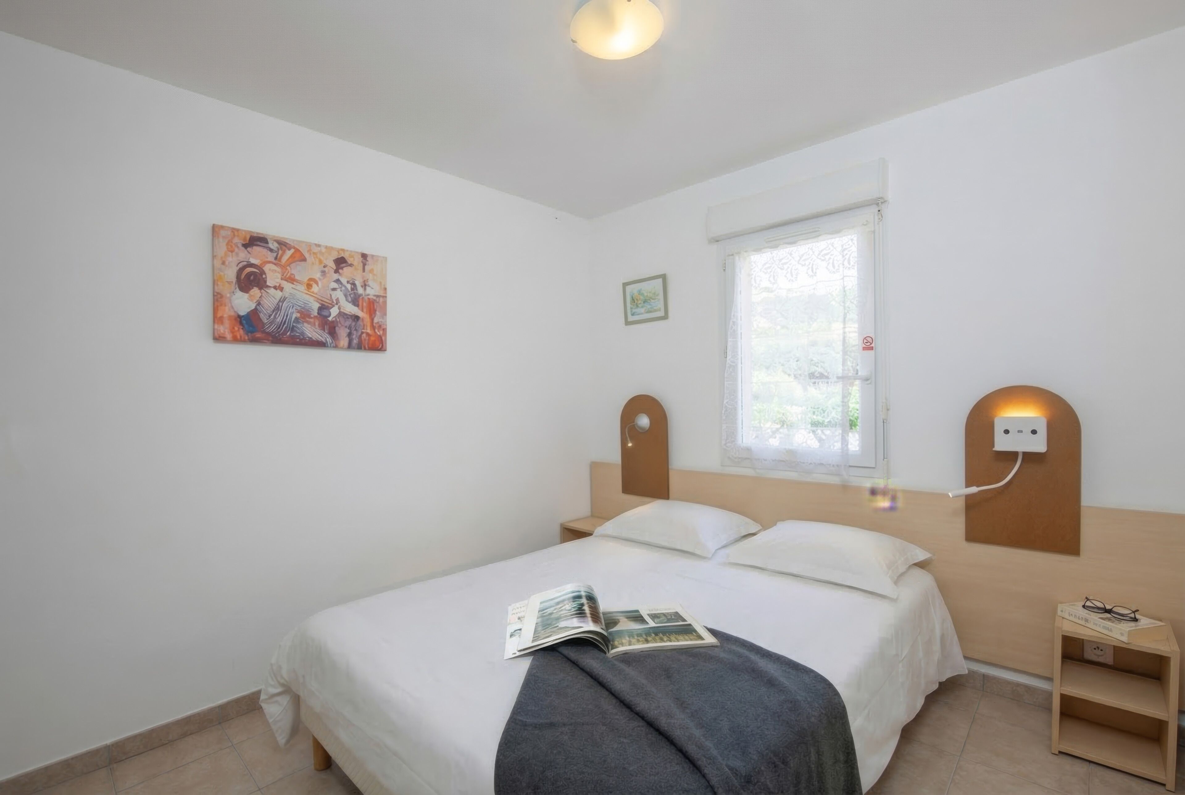 Una camera da letto con un letto, un comodino, una lampada a parete, una finestra e un quadro.