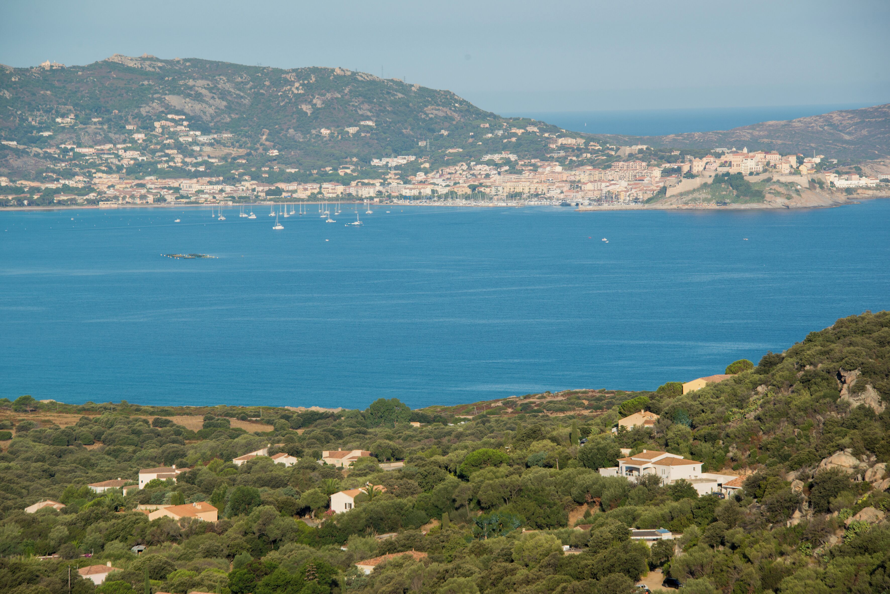 Un pueblo costero con edificios, un mar azul cristalino y un paisaje montañoso.