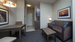 A hotel room with a dining table, a sofa, a small coffee table, a kitchen area, and a framed picture on the wall. - Holiday Inn Express Hotel & Suites Morgan City Tiger Island by IHG (Morgan City)