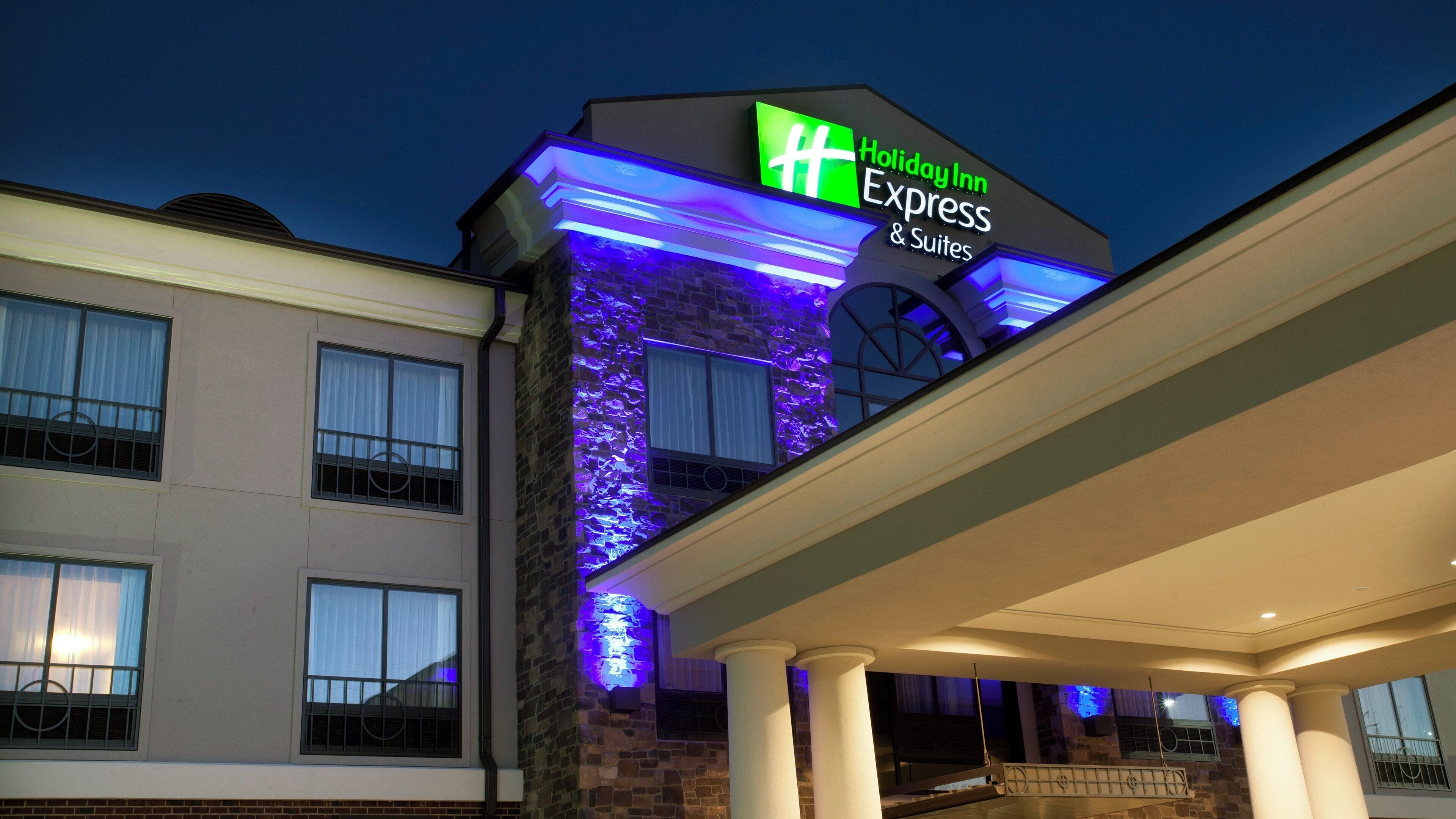 Ein Holiday Inn Express & Suites Hotel mit einer Fassade aus Stein und beleuchteter Beschilderung.