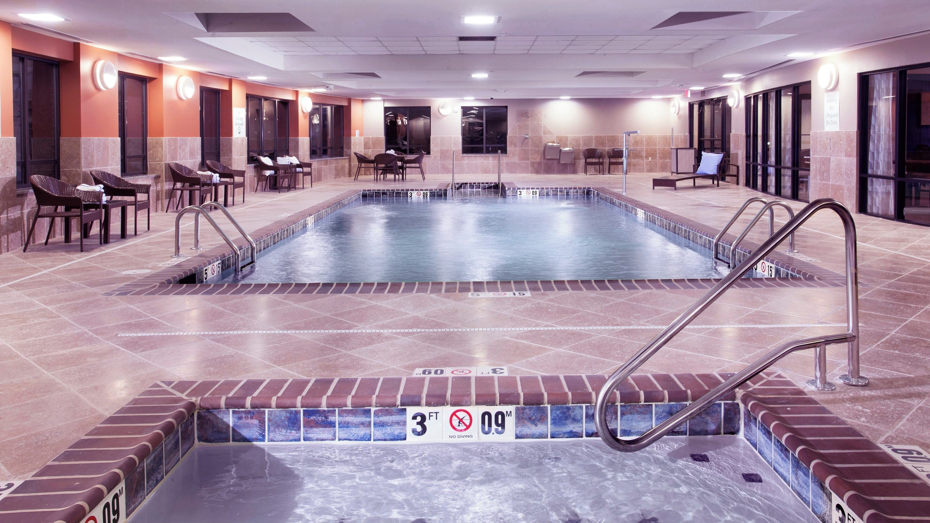 Una piscina con un letrero que indica prohibido bucear, sillas de descanso y piso de baldosas.