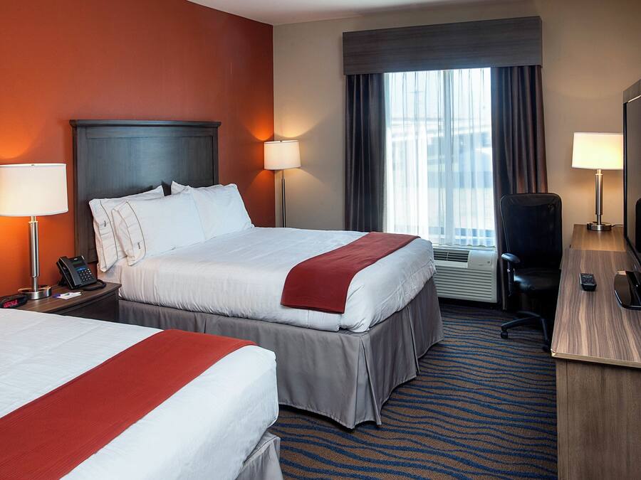 Ein Hotelzimmer mit zwei Betten, einem Schreibtisch, einem Stuhl, einem Fernseher und einem Fenster mit Vorhängen.