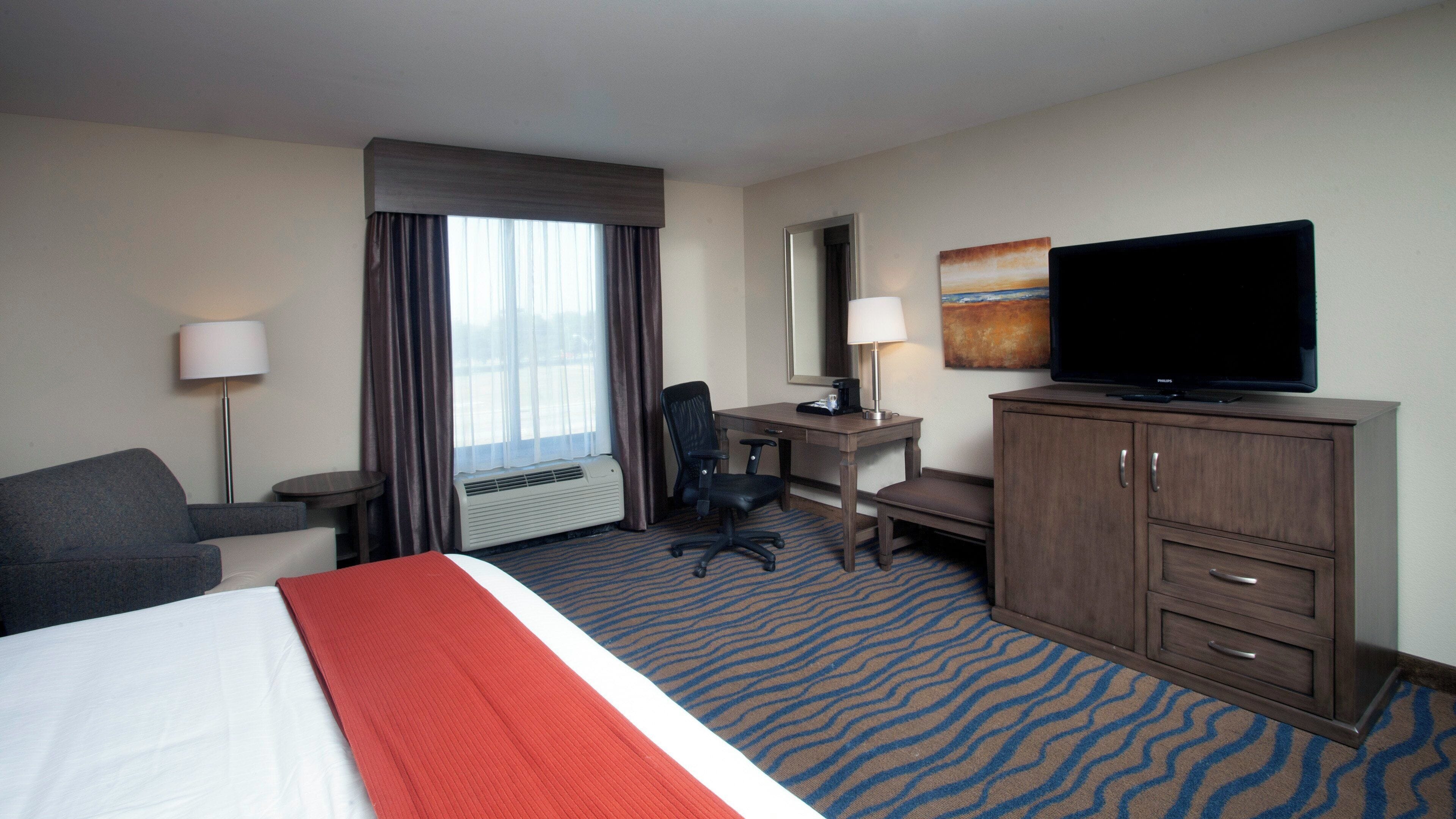 A hotel room with a bed, desk, chair, television, and a large window with curtains.