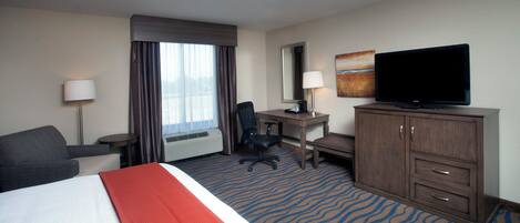 A hotel room with a bed, desk, chair, television, and a large window with curtains.