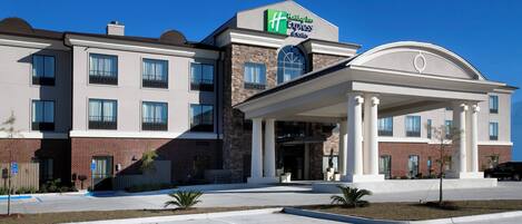 Ett Holiday Inn Express & Suites-hotell med en fasad av tegel, stora fönster och en överbyggd entré.