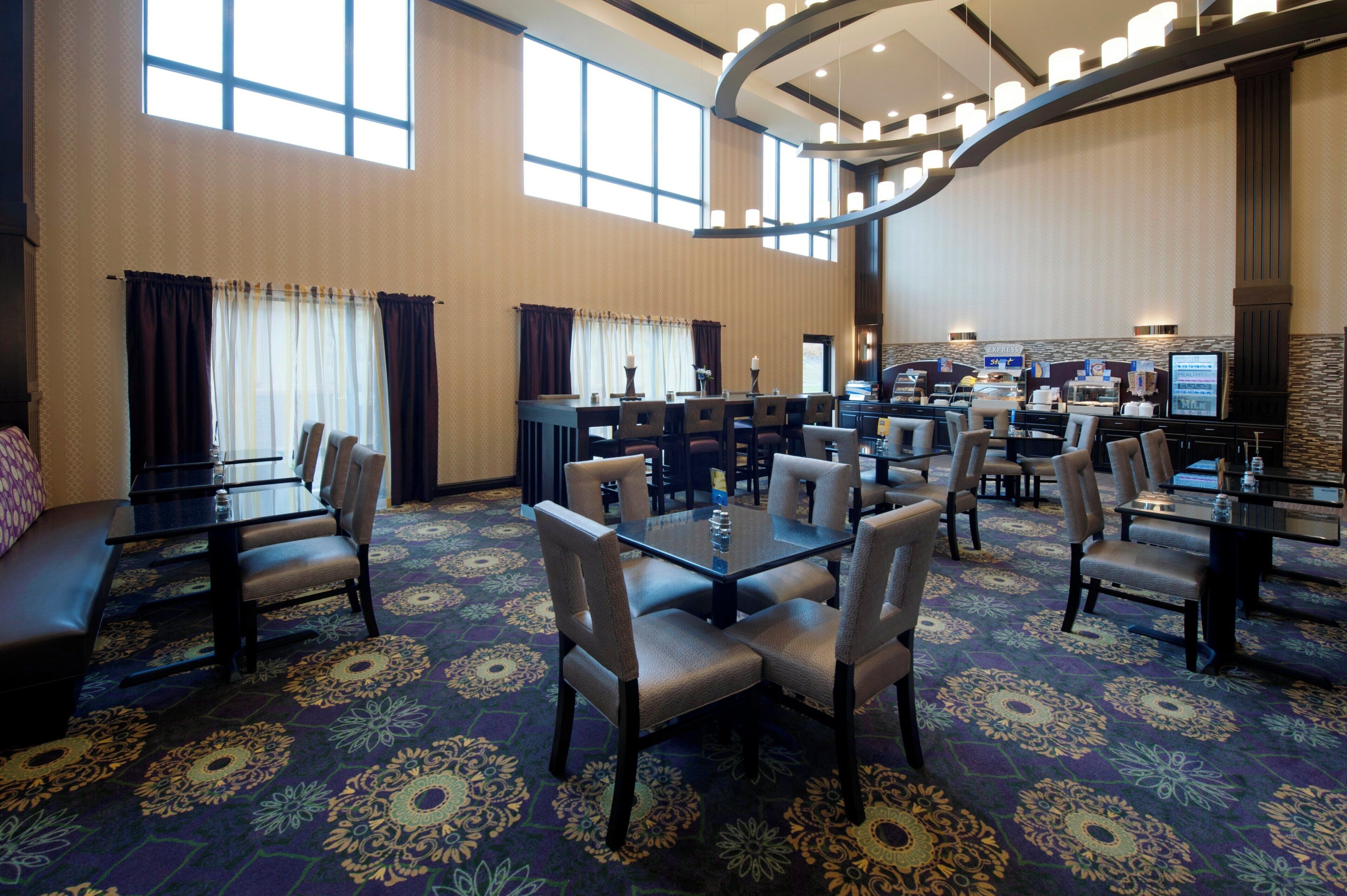 Un comedor de hotel con varias mesas y sillas, un candelabro central y vistas al área de la cocina.