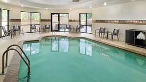 Una piscina con sillas y un banco alrededor, una pared de azulejos y una puerta que da al exterior.