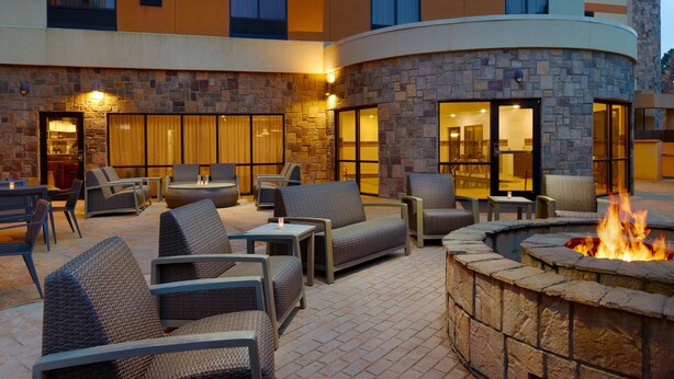 Un patio al aire libre con mobiliario de mimbre, un hogar de piedra y un edificio con grandes ventanales y una zona de bar.