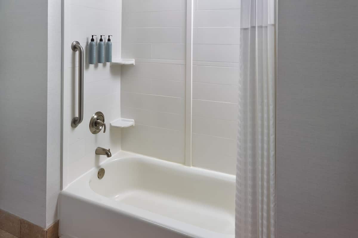 Une salle de bain avec une baignoire blanche, des barres d’appui et une étagère contenant des articles de toilette.