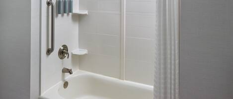 A bathroom with a white bathtub, grab bars, and a shelf with toiletries.