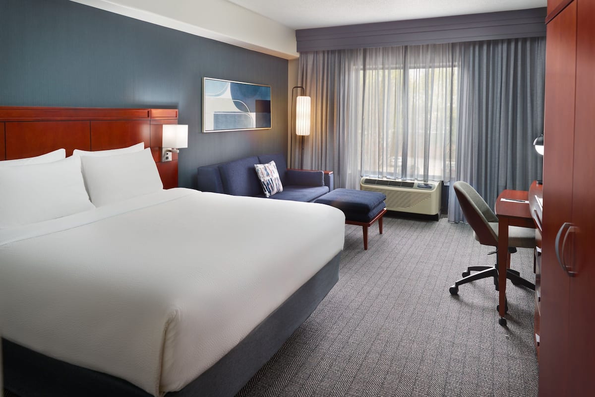 Quarto de hotel com uma cama grande, um sofá, uma escrivaninha e um aparelho de ar condicionado.