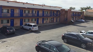 Un motel de varios pisos, con puertas azules y un estacionamiento con varios autos.