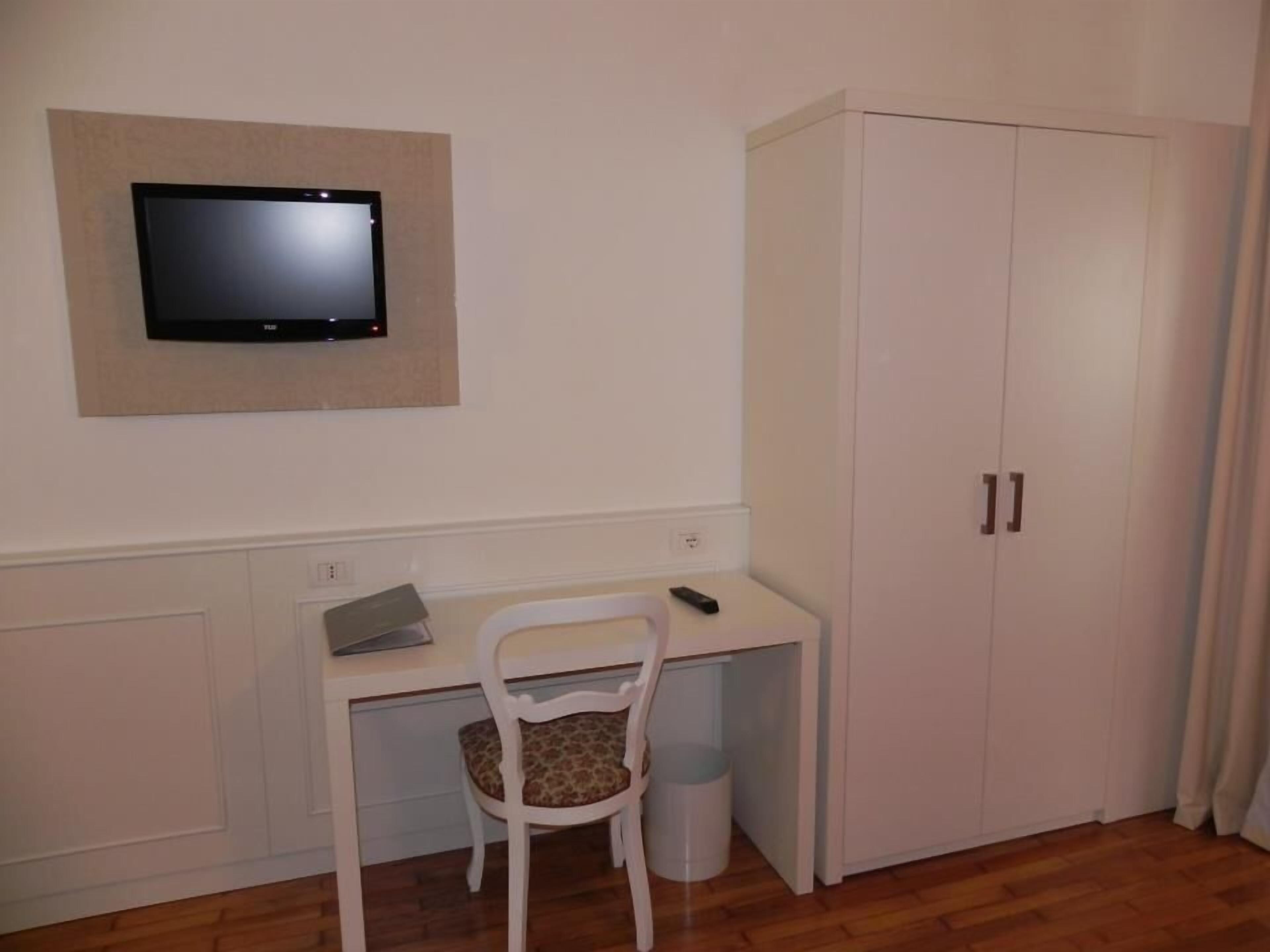 A room with a desk, chair, television, wardrobe, and a trash bin.