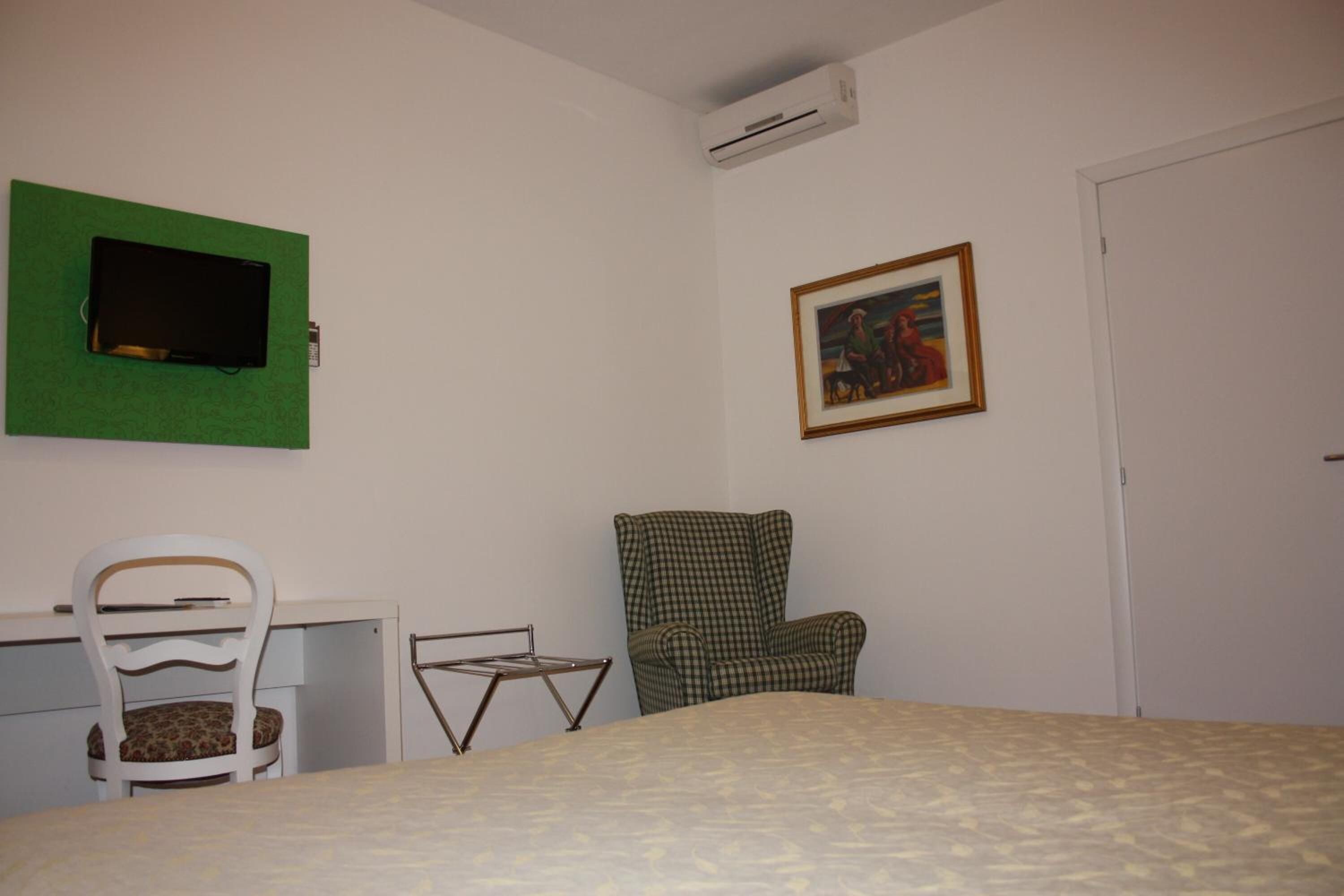 Una camera da letto con un letto, una scrivania con una sedia, una TV verde a parete, un quadro incorniciato e un condizionatore d'aria.