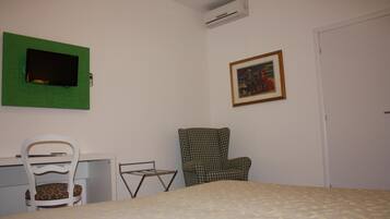 Una camera da letto con un letto, una scrivania con una sedia, una TV verde a parete, un quadro incorniciato e un condizionatore d'aria.