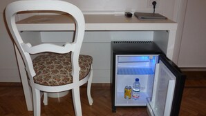 A compact refrigerator with a water bottle and a can inside, placed next to a white chair with a floral cushion. - Affittacamere Via Mazzini (Stresa)