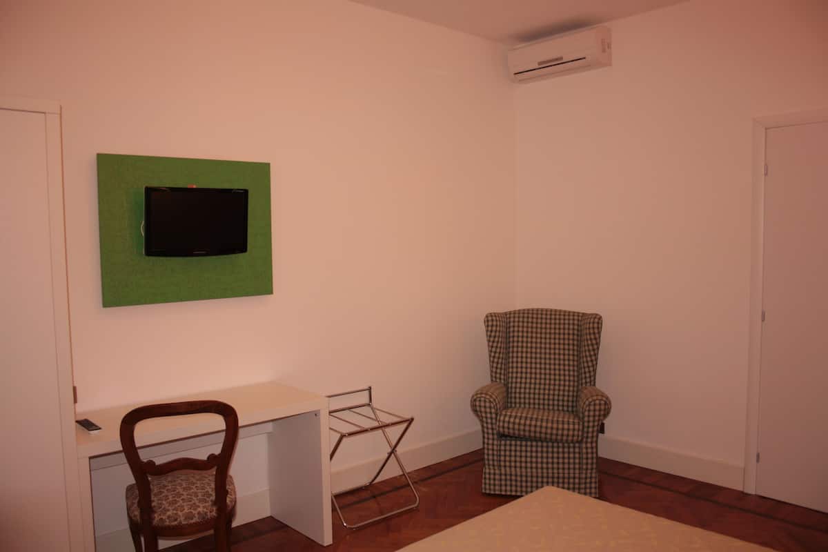 Une pièce comprenant un bureau, une chaise, un téléviseur fixé sur un panneau vert et un appareil de climatisation mural.
