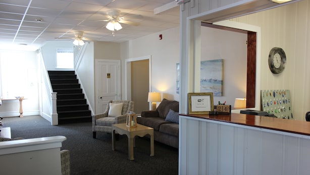 A hotel lobby with a reception desk, a staircase, a sofa, and a lamp. - Blue Water Inn (Ocean City)