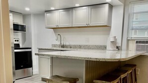 A modern kitchen with white cabinets, a granite countertop, and wooden stools. - Blue Water Inn (Ocean City)