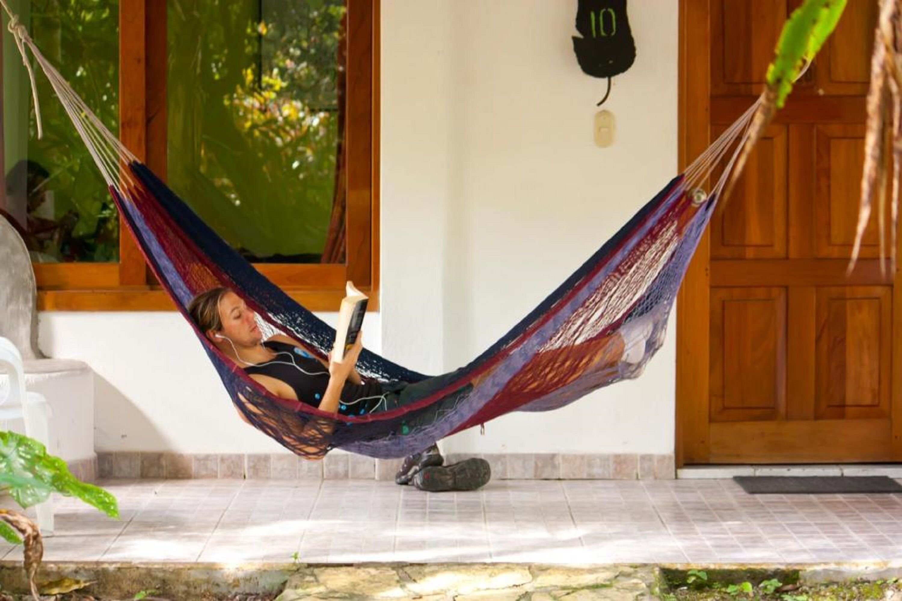 Uma pessoa relaxando em uma rede em uma varanda, com uma porta de madeira e uma janela ao fundo.