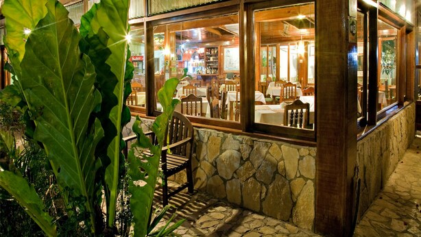 An outdoor restaurant with stone walls, wooden furniture, and large windows. - Hotel Jaguar Inn Tikal (Flores)