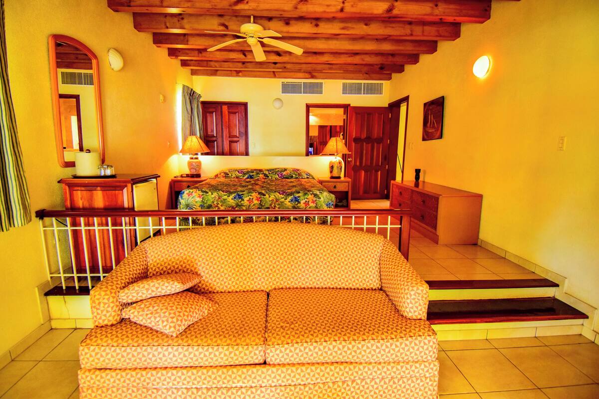 A bedroom with a bed, a sofa, a ceiling fan, and a staircase.