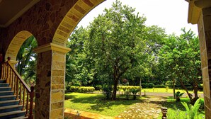 Uma escadaria de pedra leva a uma área coberta com vista para um jardim exuberante e um lago.