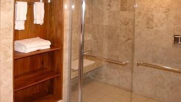 Un área de ducha con puerta de cristal, estantes de madera con toallas y suelo de baldosas.