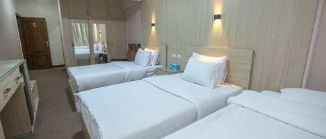 Een hotelkamer met drie bedden, een kledingkast, een spiegel en een kleine tafel met een blauw voorwerp erop.