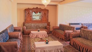 A living room with brown leather sofas, a patterned rug, a wooden cabinet with a mirror, and a chandelier. - Guardian Guest House (Giza)