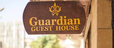 Une enseigne en bois portant l’inscription « Guardian Guest House » est suspendue à un bâtiment.