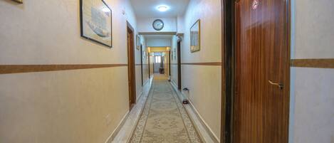 Un pasillo de hotel con piso alfombrado, puertas de madera y cuadros en las paredes.